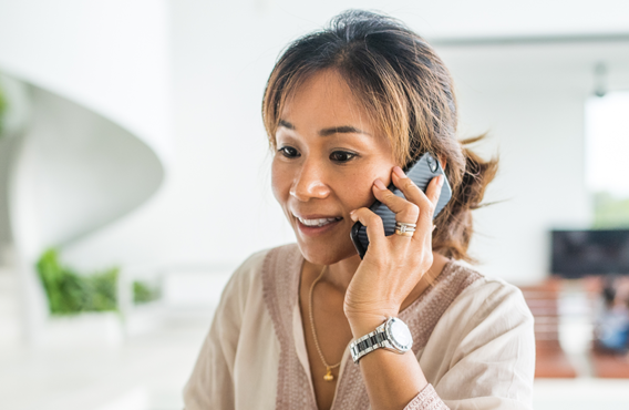 A woman in front of a bright blurred background, talking on her phone.