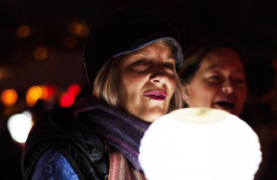 Old woman holding a white lit lamp at night