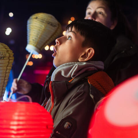 A young boy and a woman both with shocked expressions, holding lanterns, and looking at something off camera